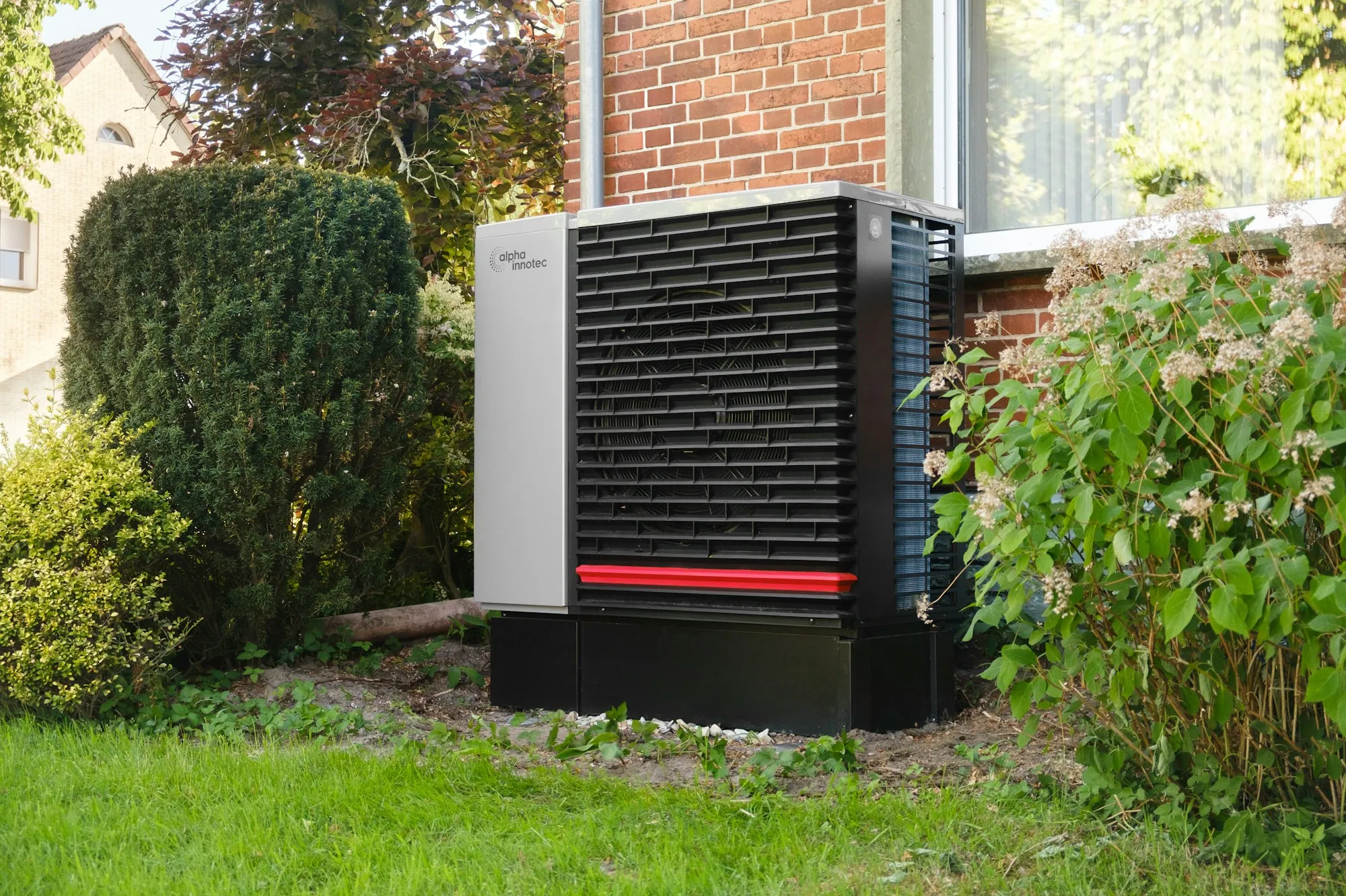 Heat pump unit on green grass beside garden hedges
